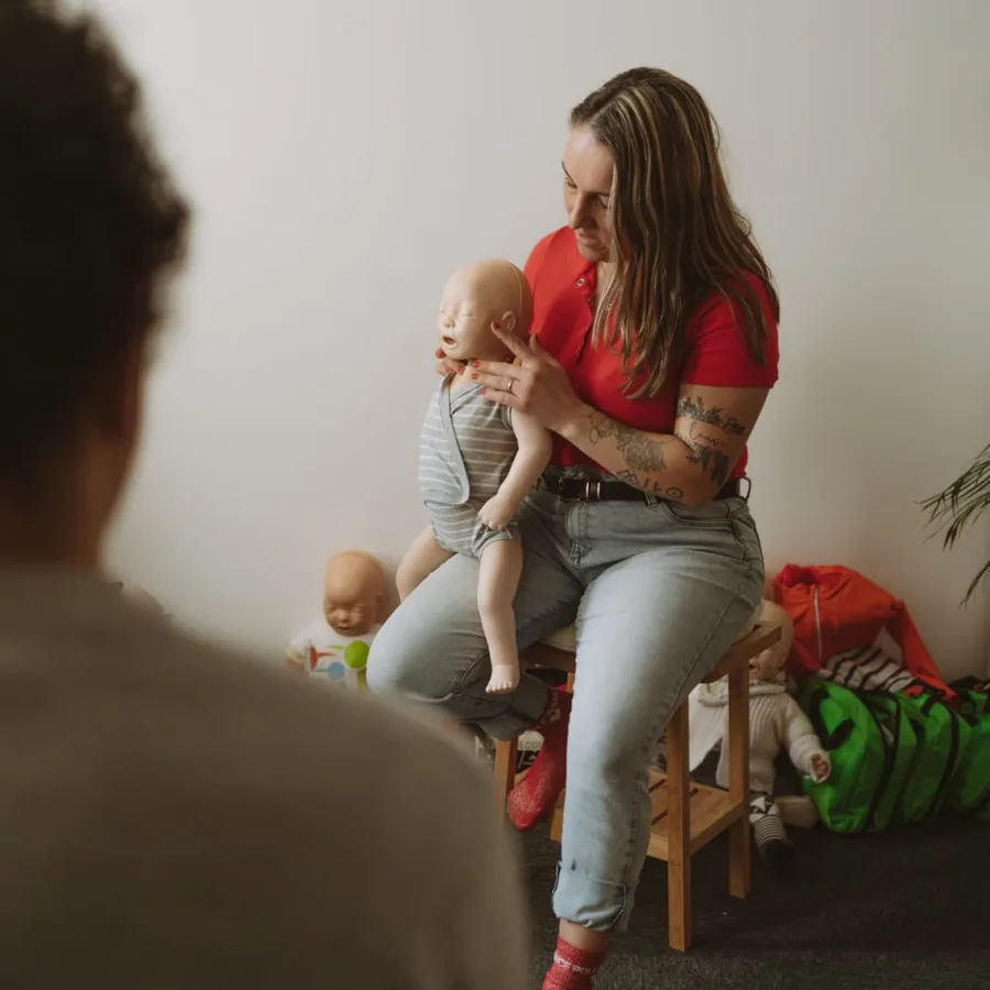 Une formatrice Famille de Sauveteurs montre à des parents comment tenir un nourrisson, sur un mannequin de secourisme