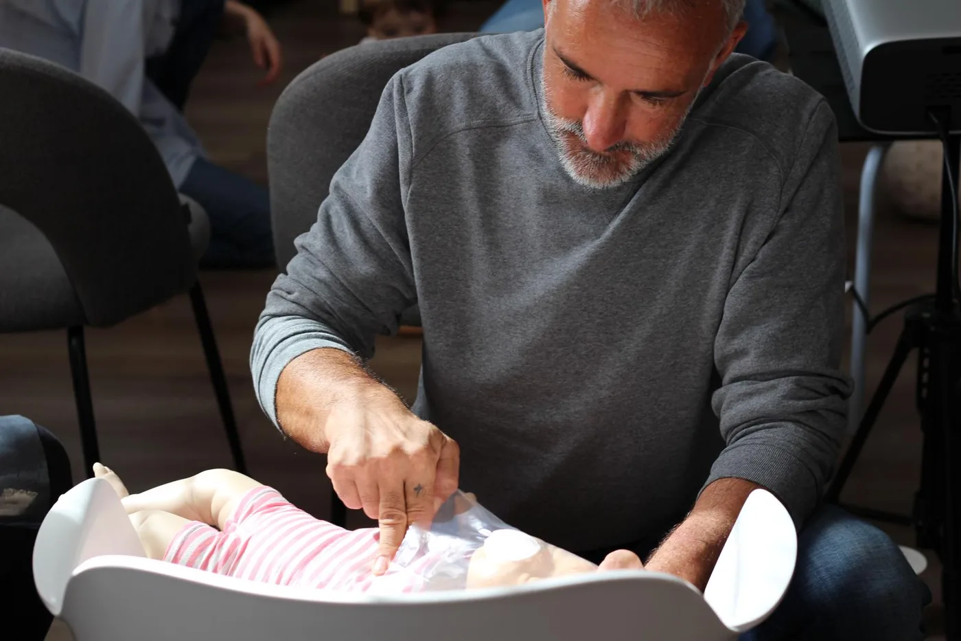 Un grand-père s'exerce aux compressions thoraciques sur un mannequin nourrisson pendant une formation Famille de Sauveteurs