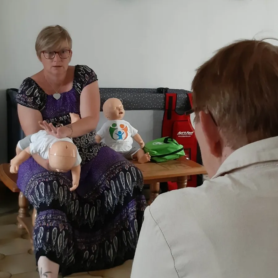 Cécile Tiscornia montre les claques dans le dos sur un mannequin nourrisson, face à un participant, dans son salon