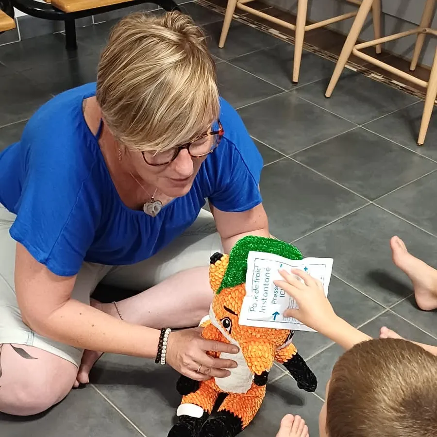 Cécile Tiscornia pose une poche de froid sur Rescue, la peluche renard, avec un enfant assis par terre