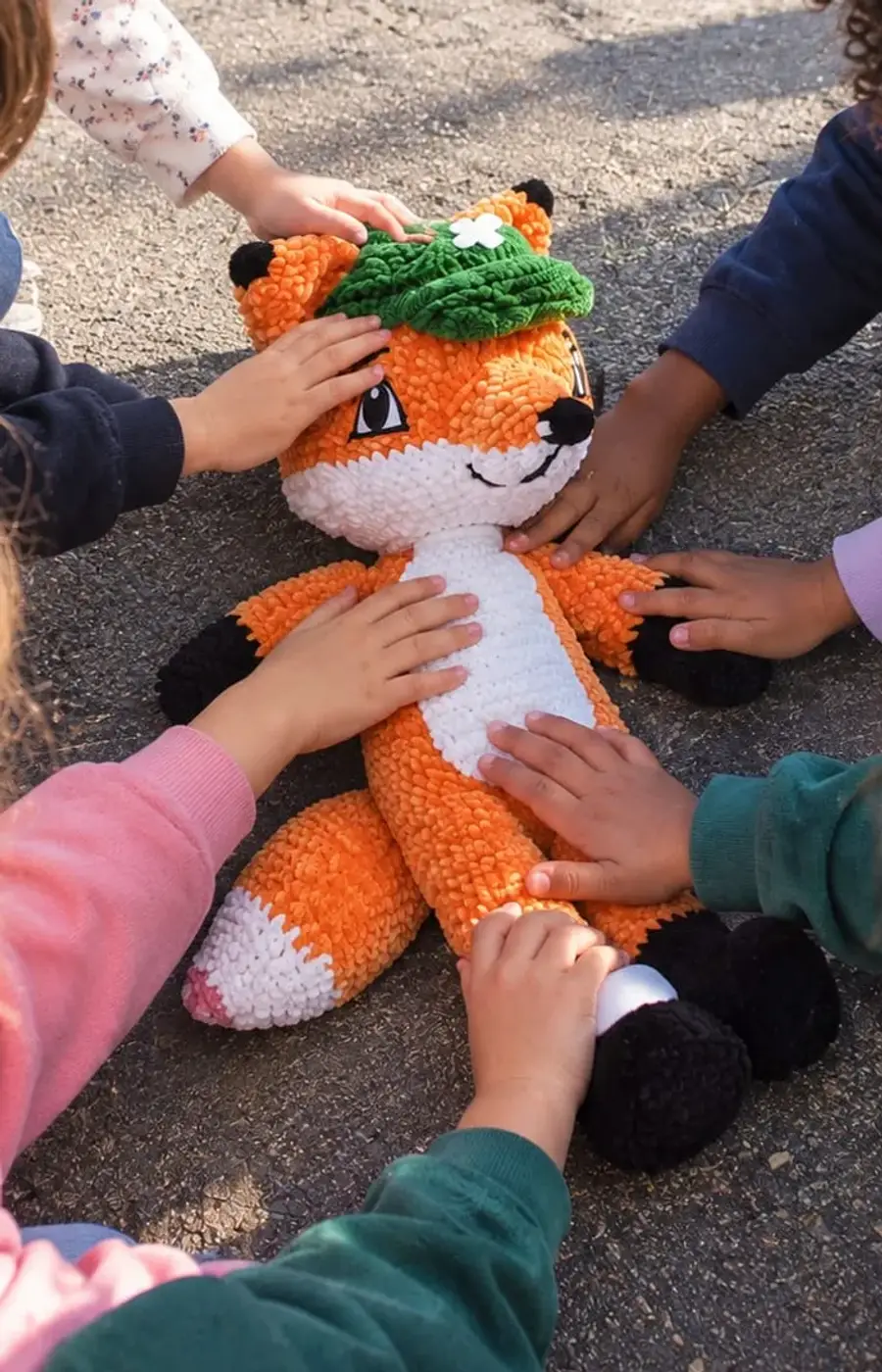 Des enfants accroupis dans une cour d'école, les mains posées sur Rescue le Renard, la peluche grandeur nature de Famille de Sauveteurs